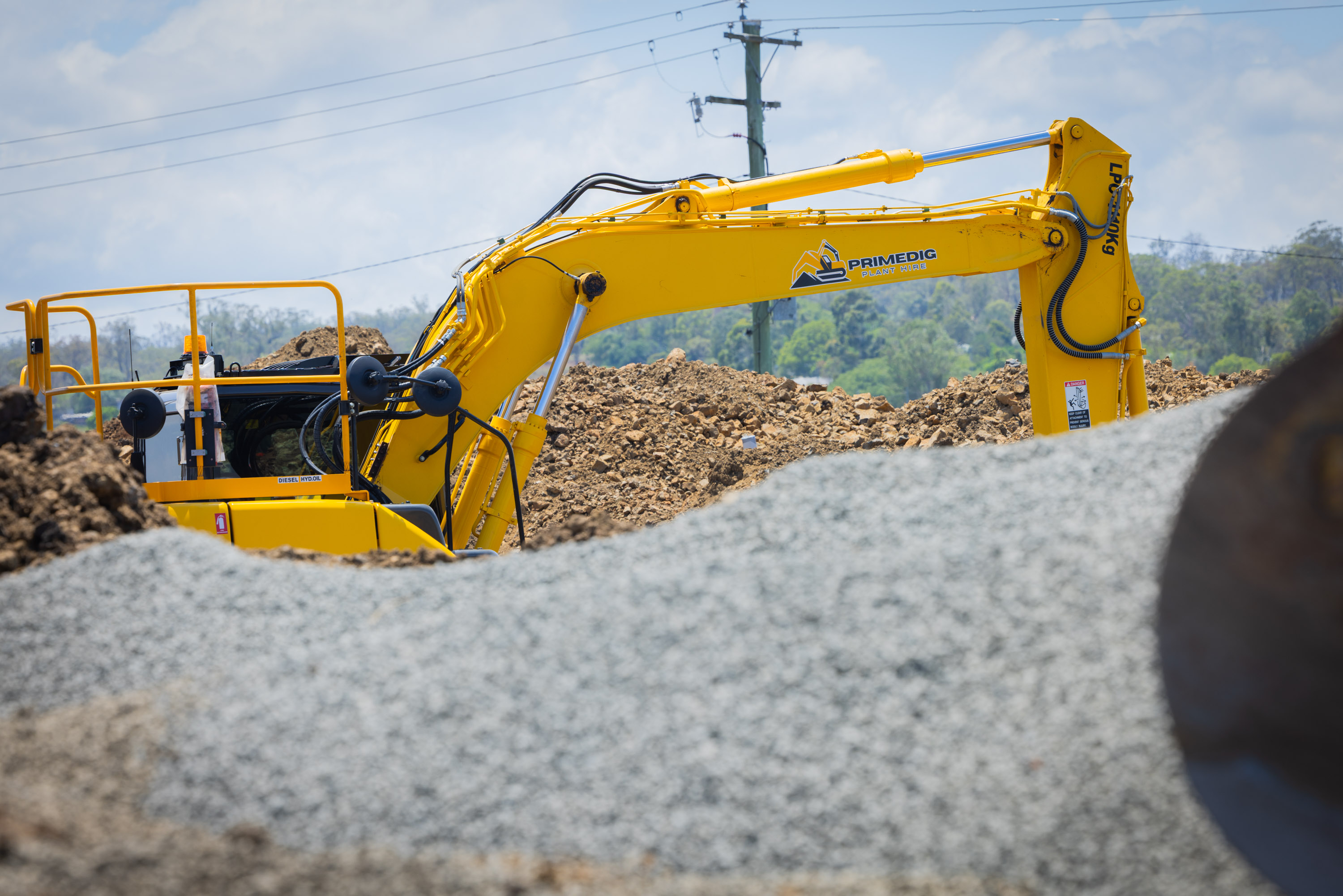 Sumitomo excavator working behind a gravel stockpile on a Brisbane job site